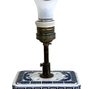 May include: A blue and white porcelain table lamp with a dragon design. The lamp has a white globe shade and a brass finial. The base of the lamp is square and sits on a wooden base.