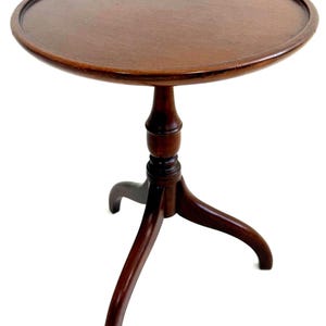 May include: A dark brown, round side table with a three-legged base. The tabletop is circular with a raised edge. The table is made of wood and has a classic, antique design. The table is approximately 24 inches in diameter.