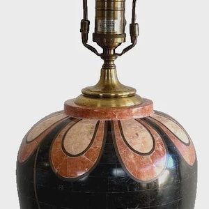 May include: A table lamp with a tall, vase-shaped body featuring black, pink, and cream stone inlay in a leaf pattern. The lamp has a brass base, a brass harp, a brass finial, and a single white light bulb centered in the socket assembly.