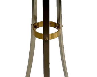 May include: A decorative plant stand with a round glass top. The stand features gold-colored ram's head accents and a gold-colored ring around the center. The legs are silver-colored with gold-colored feet.