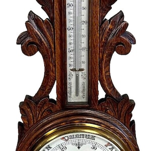 May include: A vintage wooden barometer with a thermometer and an aneroid barometer. The barometer has a round face with a needle pointing to the current air pressure. The face is labeled with the words "Stormy", "Rain", "Change", "Fair", and "Very Dry". The thermometer is labeled in degrees Fahrenheit. The barometer is mounted on a wooden plaque with ornate carvings.