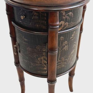 May include: A dark brown, antique side table with a round top and a lower cabinet. The cabinet features a black background with a gold landscape design. The table has bamboo-style legs and supports.