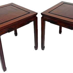 May include: Two square, dark wood side tables with a rich, reddish-brown finish. Each table has a recessed top with a dark border and ornate carvings on the apron. The legs are straight and taper slightly towards the bottom. The tables are approximately 24 inches tall.