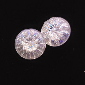 May include: Two clear, round earrings with a detailed, leaf-like pattern. The earrings have a central, clear, round gem. The background is black.