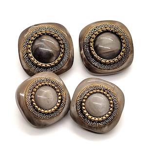 May include: Four square-shaped buttons with a marbled gray center, surrounded by a gold-colored beaded ring and a bronze-colored frame. The buttons have a slightly rounded shape and are set against a white background.
