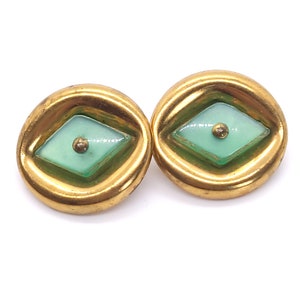 May include: A pair of vintage gold-tone earrings. Each earring features a round, gold-colored frame with a light green, diamond-shaped center. A small, gold-colored stud is in the center of each diamond.
