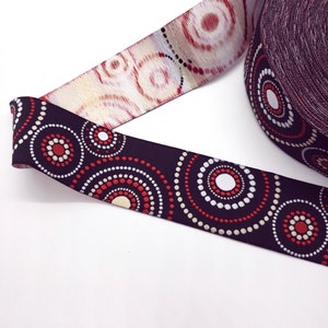 May include: Decorative ribbon with a repeating pattern of red, white, and beige circles on a dark background. A roll of ribbon is visible, with a section unrolled, showing the design. The ribbon is likely used for crafts or gift wrapping.