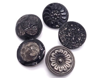 May include: A collection of six decorative buttons in various designs and finishes. The buttons are primarily black, with some featuring silver or speckled details. The designs include floral patterns and textured surfaces, suitable for sewing or crafts.