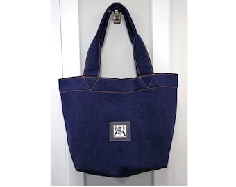 May include: A dark blue denim tote bag with orange stitching and a small square patch with a design on the front.