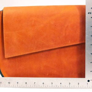 K&ouml;nnte beinhalten: Eine braune Ledertasche mit einem Klappverschluss und schwarzem Besatz. Die Tasche ist etwa 23 cm hoch.