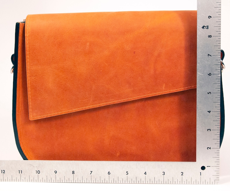 K&ouml;nnte beinhalten: Eine braune Ledertasche mit einem Klappverschluss und schwarzem Besatz. Die Tasche ist etwa 23 cm hoch.