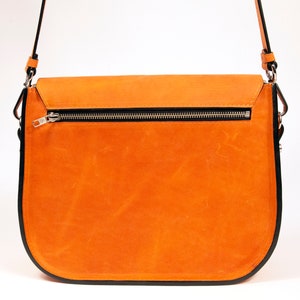 K&ouml;nnte beinhalten: Eine braune Ledertasche mit schwarzem Besatz und einem silbernen Rei&szlig;verschluss. Die Tasche hat einen langen Riemen und einen Klappverschluss.