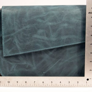 May include: A teal blue leather crossbody bag with a flap closure. The bag has a rounded bottom and a silver chain strap.