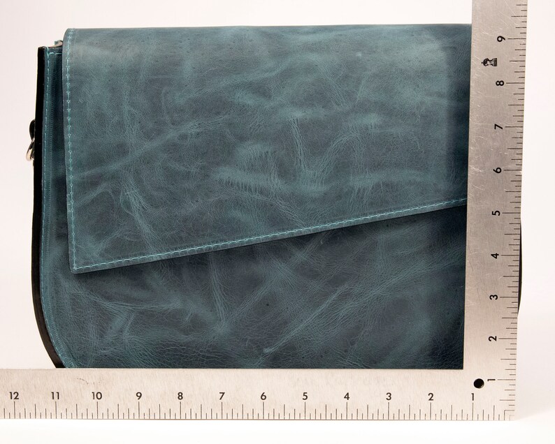 May include: A teal blue leather crossbody bag with a flap closure. The bag has a rounded bottom and a silver chain strap.