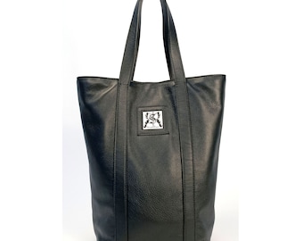May include: A black leather tote bag with two long handles. The bag has a textured surface and a rectangular silver emblem on the front. The bag is designed with vertical seams and a spacious interior.