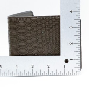 May include: A brown leather wallet with a snakeskin pattern. The wallet is measured with a ruler, showing it is about 3 inches wide.