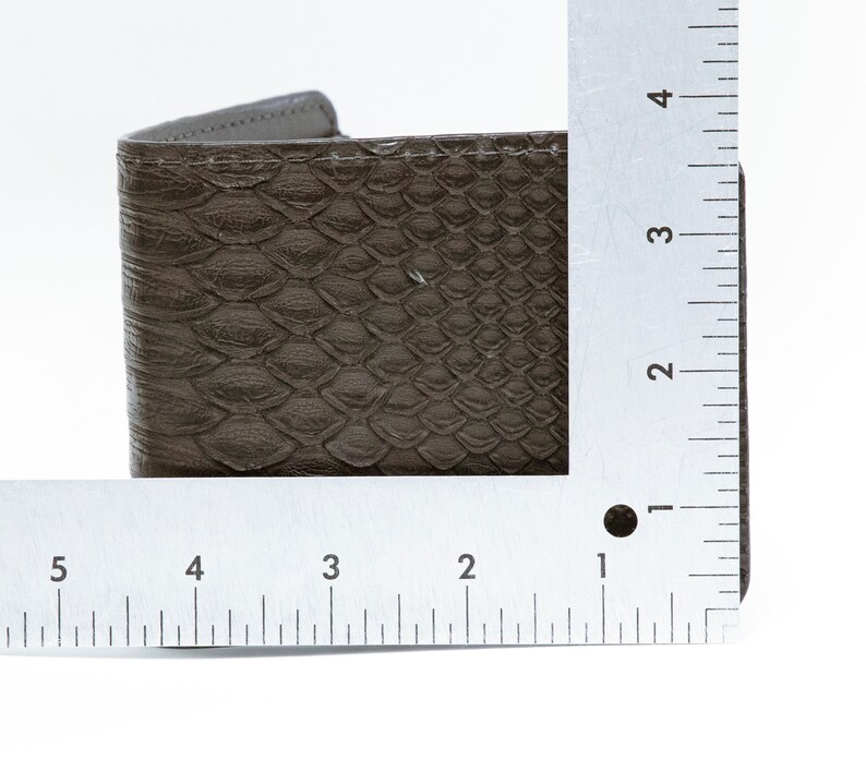 May include: A brown leather wallet with a snakeskin pattern. The wallet is measured with a ruler, showing it is about 3 inches wide.