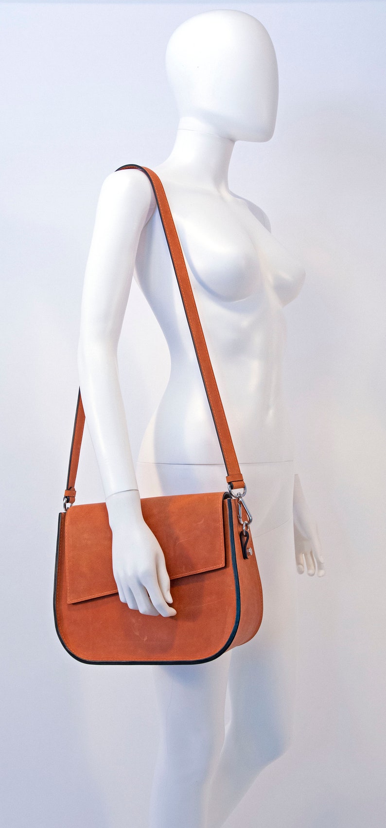 K&ouml;nnte beinhalten: Eine braune Lederschultertasche mit Klappenverschluss und einem silbernen Verschluss. Die Tasche hat einen langen verstellbaren Riemen.