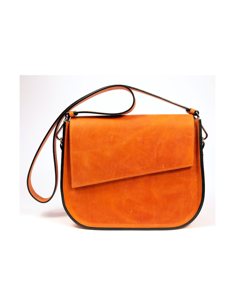 K&ouml;nnte beinhalten: Eine braune Lederschultertasche mit schwarzem Besatz. Die Tasche hat einen Klappenverschluss und einen langen verstellbaren Riemen.