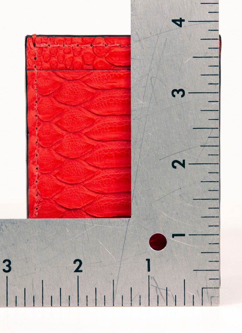 Puede incluir: Una cartera de cuero roja con un patr&oacute;n texturizado de piel de serpiente. La cartera se mide con una regla, mostrando que mide aproximadamente 7,6 cm de ancho y 10,2 cm de alto.