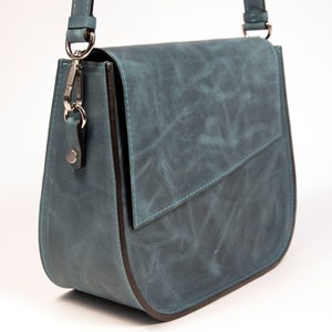 May include: A teal blue leather shoulder bag with a flap closure and a silver clasp. The bag has a dark brown trim around the edges.