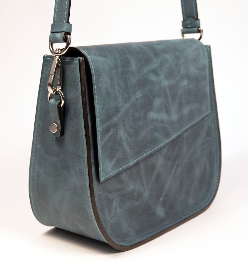 May include: A teal blue leather shoulder bag with a flap closure and a silver clasp. The bag has a dark brown trim around the edges.