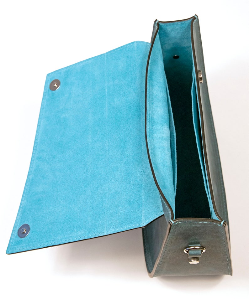 May include: A teal leather handbag with a flap top and a blue suede interior. The bag has a silver clasp and a silver strap.