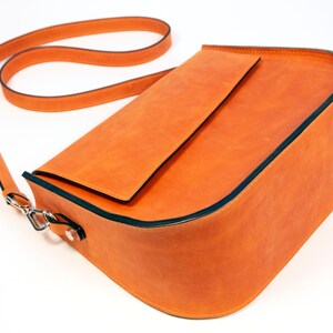 K&ouml;nnte beinhalten: Eine leuchtend orangefarbene Lederschultertasche mit schwarzem Besatz und einem langen Trageriemen. Die Tasche hat einen Klappenverschluss und ein kleines Fach auf der Vorderseite.