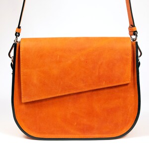 K&ouml;nnte beinhalten: Eine braune Ledertasche mit schwarzem Besatz und einem Klappverschluss. Die Tasche hat einen langen Riemen zum Tragen &uuml;ber der Schulter.