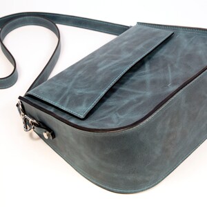 May include: A teal blue leather shoulder bag with a flap closure and a small pocket on the front. The bag has a long adjustable strap.