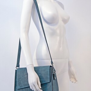 May include: A blue leather shoulder bag with a flap closure and a long adjustable strap.