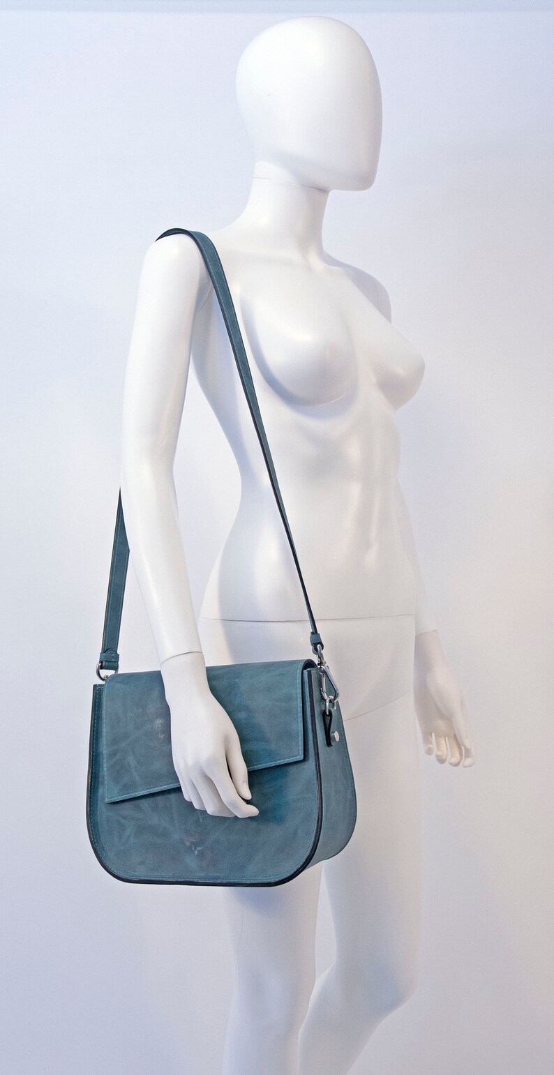 May include: A blue leather shoulder bag with a flap closure and a long adjustable strap.