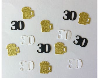 May include: A collection of party confetti pieces featuring the number 30 in black and white cardstock, alongside gold glitter cardstock shapes resembling beer mugs. The pieces are scattered across the frame in a random arrangement.
