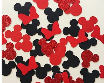 May include: A collection of paper confetti shapes including black mouse head silhouettes, solid red mouse head silhouettes, red glitter mouse head silhouettes, and solid red bows scattered across a plain, light-colored surface.
