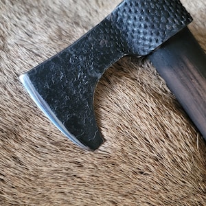 May include: A black axe with a textured handle and a sharp blade. The axe is resting on a brown fur surface.
