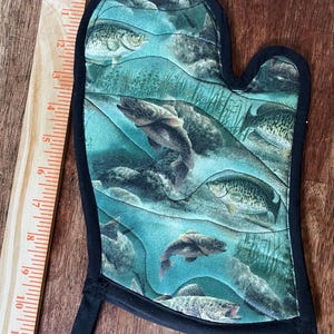 May include: An oven mitt with a black trim and loop. The mitt features a teal and blue underwater scene with various fish. The design includes fish swimming among rocks and aquatic plants. The mitt is approximately 10 inches long.