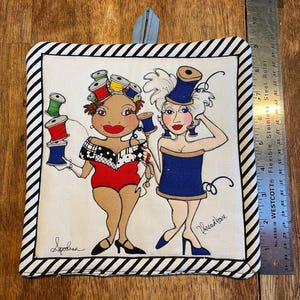 May include: A white cotton hot pad with black and white stripes. The hot pad features a colorful illustration of two women dressed as spools of thread. The text "Spodiva" and "Phreadbare" are written on the hot pad.