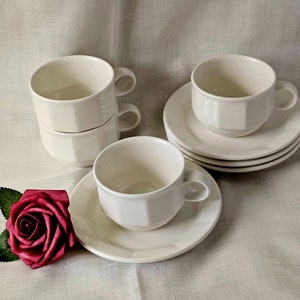 Könnte beinhalten: Set aus vier weißen Keramik-Teetassen und Untertassen. Die Tassen haben ein schlichtes, elegantes Design mit einem leicht ausgestellten Rand. Die Untertassen sind etwas größer als die Tassen und haben ein passendes Design.