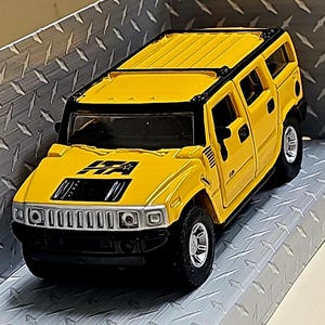 Può includere: Un Hummer H2 SUV giocattolo giallo con finiture nere e una griglia nera. Il giocattolo ha un portapacchi da tetto nero e un emblema "H2" nero sul lato.