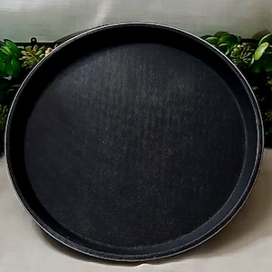 Può includere: Una teglia rotonda nera con una superficie strutturata e un bordo argentato. La teglia è progettata per cuocere al forno. Il diametro della teglia è di circa 30 cm.