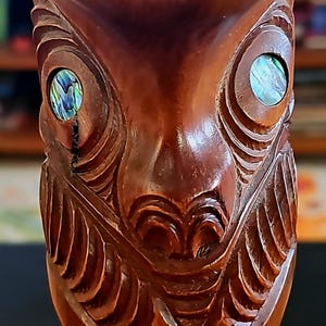 Könnte beinhalten: Eine geschnitzte Tiki-Statue aus Holz mit komplizierten Details. Die Statue hat eingelegte irisierende Augen und detaillierte Gesichtszüge. Das Holz hat eine satte, dunkelbraune Farbe, und der Schnitzstil ist traditionell.