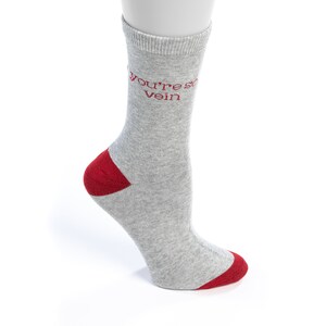 May include: Gray crew socks with a red heel and toe. The socks have the text "You're so vein" written in red on the front.