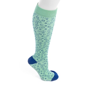 May include: A compression sock in a light green color with a pattern of blue shapes. The sock has a blue heel and toe, and a light green cuff. The sock is designed to be worn on the lower leg.