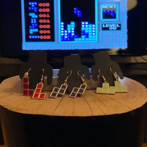 Könnte beinhalten: Vier Paar Tetris-Ohrringe. Die Ohrringe sind aus goldenem Metall und zeigen verschiedene farbige Tetris-Blöcke. Die Blöcke sind rot, blau und grün.