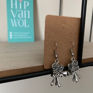 Op de afbeelding: Zilveren oorbellen in de vorm van vintage filmcamera's. Een camera heeft het woord "MOVIE" erop.