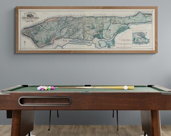 May include: A green felt pool table with a brown wooden frame and legs. There are billiard balls on the table and a pool cue on the table. A framed map of New York City hangs on the wall behind the pool table.