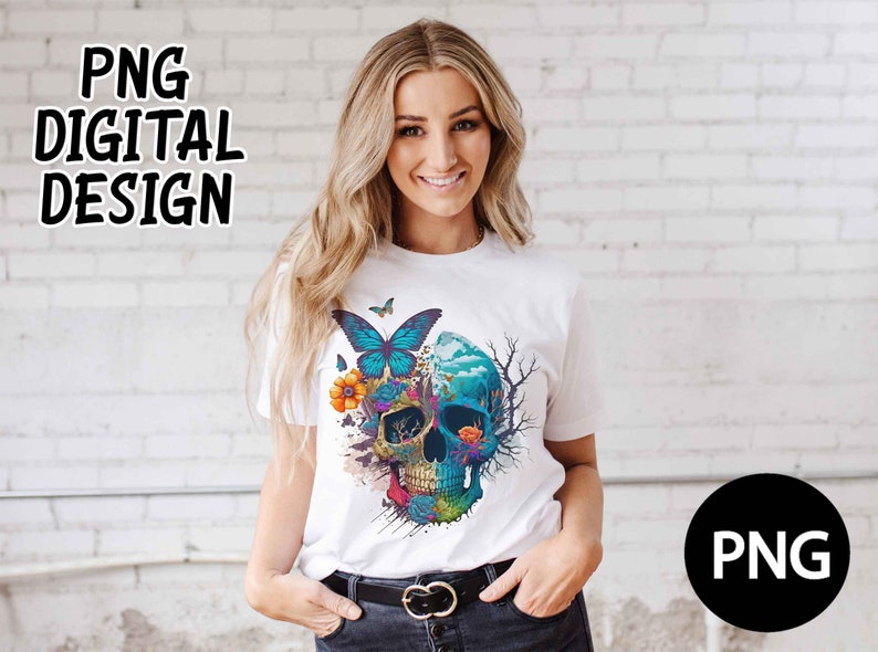 Op de afbeelding: Een wit T-shirt met een kleurrijk schedelontwerp met vlinders, bloemen en een blauw en groen landschap. De schedel is omgeven door een zwarte omtrek en heeft een witte achtergrond.