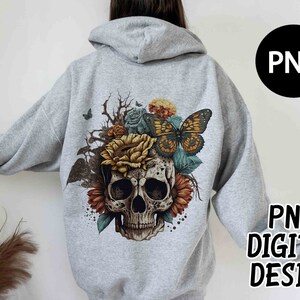 May include: A light gray hoodie featuring a detailed graphic of a skull adorned with sunflowers, roses, and a butterfly. The design includes the text "PNG DIGITAL DESIGN" in black. The hoodie has a hood and long sleeves.
