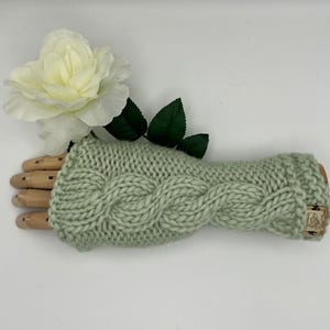 May include: A pair of sage green knitted fingerless gloves with a cable knit pattern.