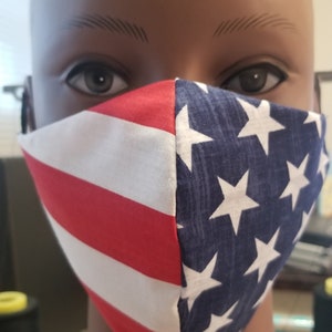 May include: A face mask with a red, white, and blue American flag design. The mask is made of fabric and has a vertical seam down the center.